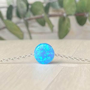 May include: A delicate silver chain necklace with a single round blue opal pendant.
