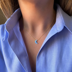 Puede incluir: Un collar de cadena dorada con un colgante de media luna de ópalo azul.