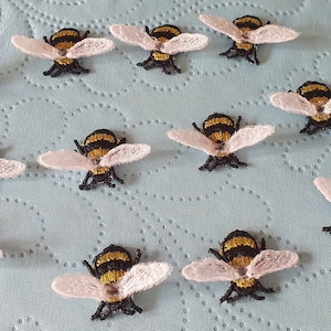 May include: Embroidered bee patches with black, yellow, and white detailing. The bee patches have outstretched wings and are arranged on a light blue surface. Ideal for craft projects.