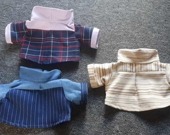 May include: Three miniature shirts with high collars. One shirt features a navy and red plaid pattern, another has blue pinstripes, and the third has horizontal tan and white stripes. The shirts are likely for a doll or small toy.