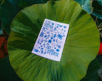 May include: A white booklet with blue illustrations and the words "go offline" is displayed on a large green lily pad. The background features lush green foliage and a red wooden structure.