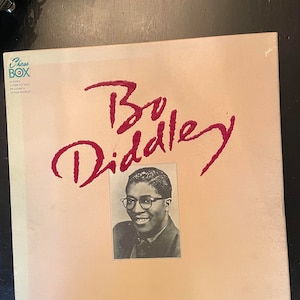 May include: A pink and white album cover with the text "Chess Box" and "Bo Diddley" in red. The album cover features a black and white photo of Bo Diddley.