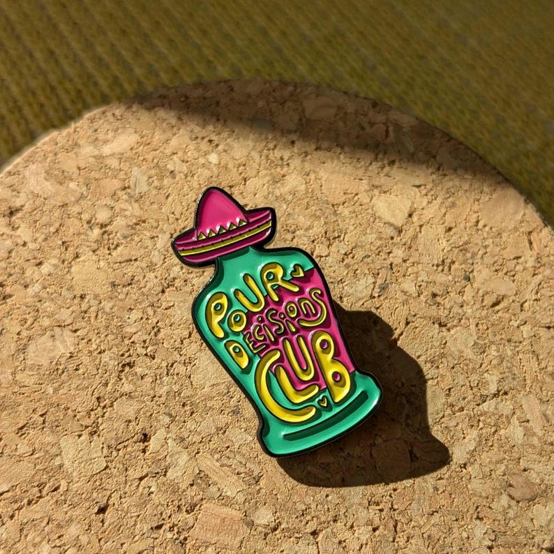 May include: A green and pink enamel pin shaped like a bottle with a sombrero on top. The bottle says "Pour Decisions Club" in yellow lettering.