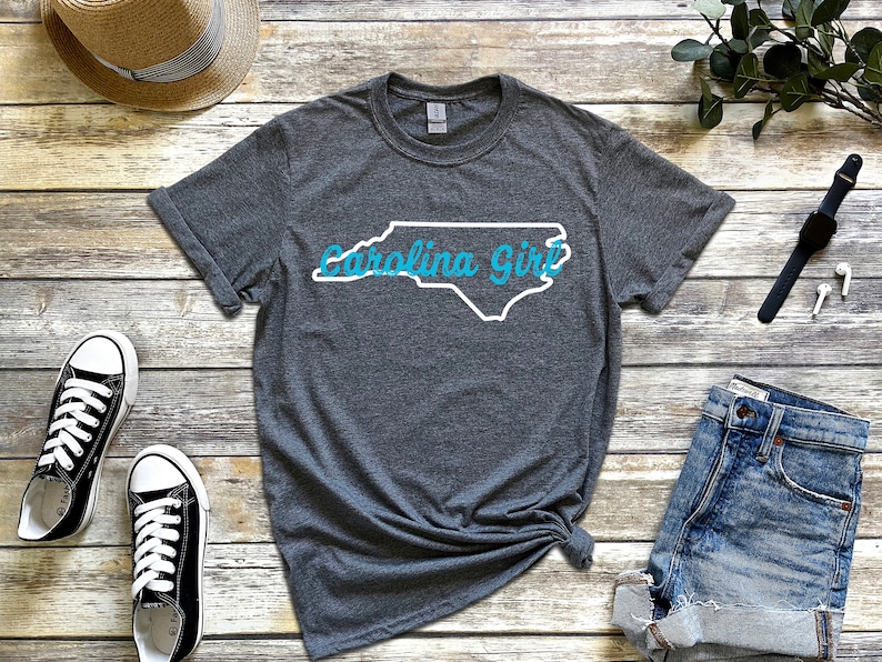 May include: A gray t-shirt with a white outline of the state of North Carolina and the text "Carolina Girl" in blue.