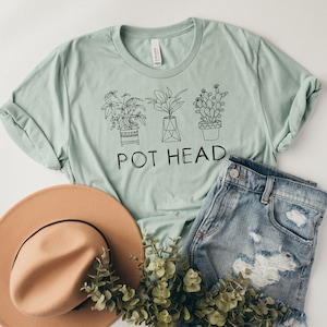 May include: A light green t-shirt with a black line drawing of three potted plants and the text "POT HEAD".