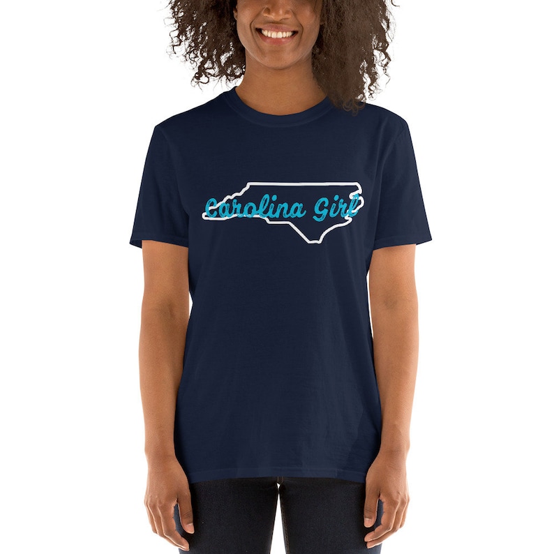 May include: A navy blue t-shirt with a white outline of the state of North Carolina and the text "Carolina Girl" in blue.