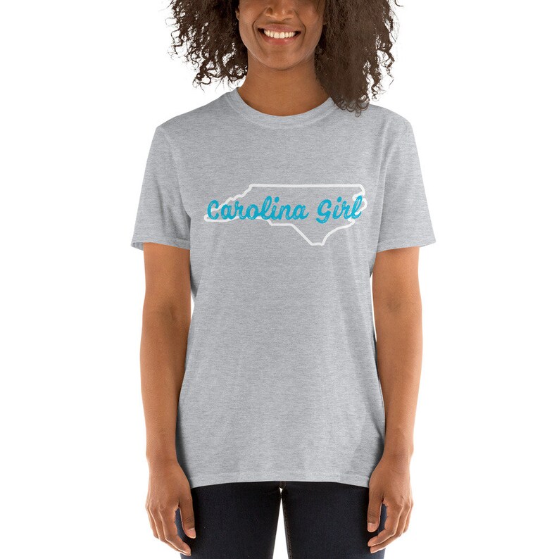 May include: A heather grey t-shirt with a white outline of the state of North Carolina and the text "Carolina Girl" in blue.