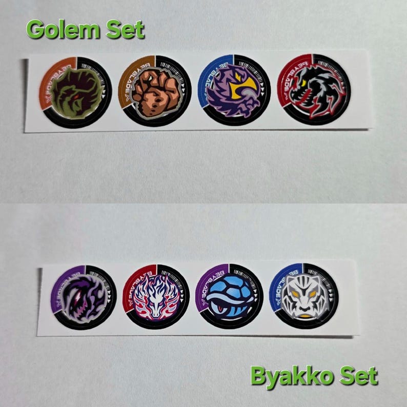 Pu&ograve; includere: Sono esposti due set di adesivi circolari. Il set superiore, etichettato "Golem Set", presenta quattro adesivi con vari disegni di mostri in arancione, marrone, viola e rosso. Il set inferiore, etichettato "Byakko Set", presenta anch'esso quattro adesivi con disegni di mostri in viola, rosso, blu e bianco.