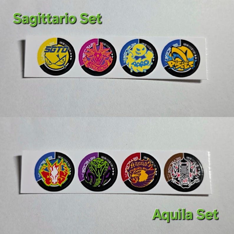 Pu&ograve; includere: Due serie di adesivi circolari, ciascuna su una striscia bianca. Il set superiore, etichettato "Sagittario Set", presenta disegni gialli, rosa e blu. Il set inferiore, etichettato "Aquila Set", presenta disegni rossi, viola e marroni. Ogni adesivo ha una grafica unica.