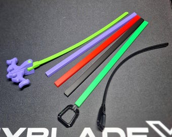 Pode incluir: Uma coleção de acessórios de brinquedo coloridos, incluindo cordas de puxar verdes, roxas, vermelhas, pretas e verdes. Um lançador roxo é visível à esquerda. O texto "YBLADE X" e caracteres japoneses são impressos na superfície.