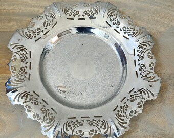 May include: A silver serving tray with a decorative, scalloped edge. The tray has a raised center and a delicate, intricate design.