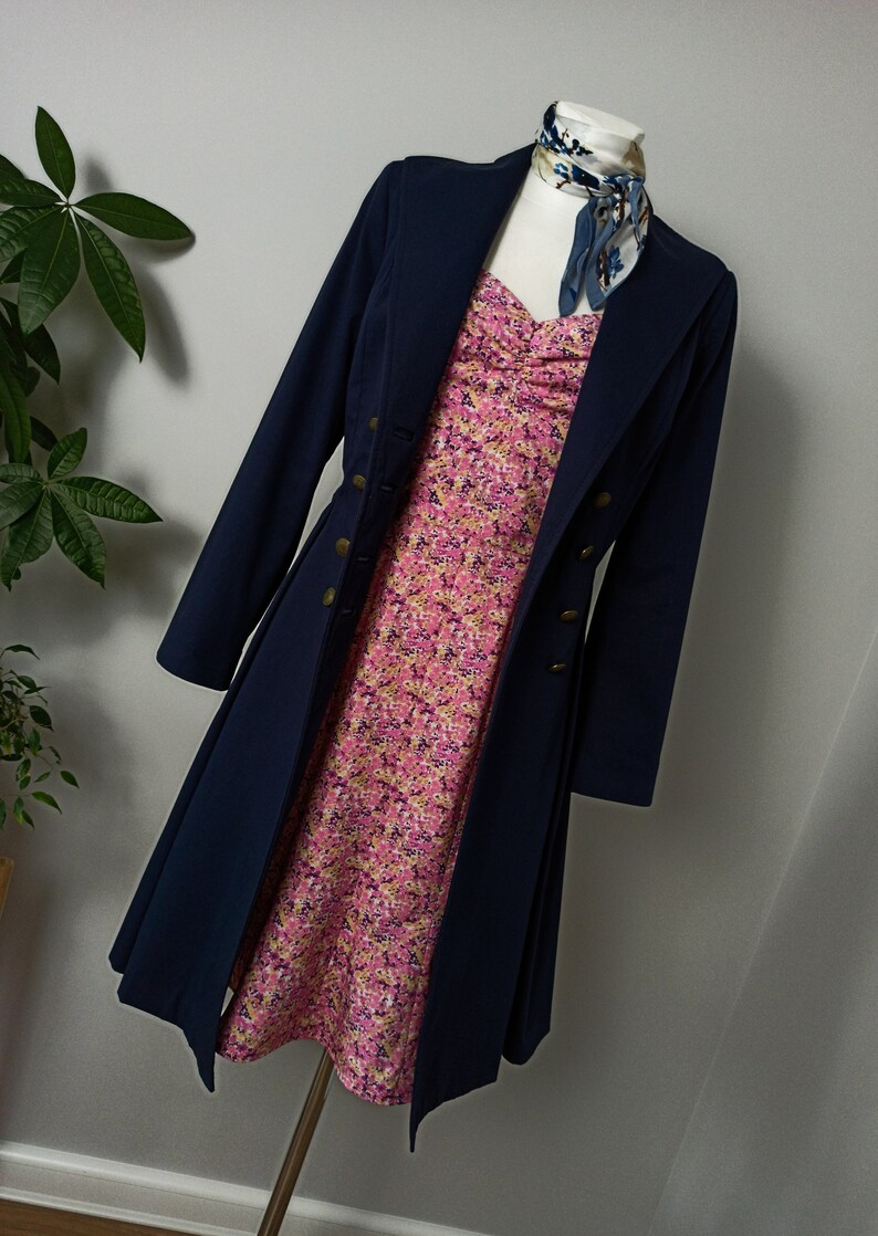 May include: A navy blue coat with gold buttons worn over a pink floral dress. The coat has a long, flowing skirt and a high collar.