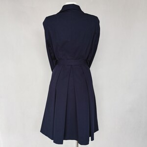May include: A navy blue dress with a collared neckline, long sleeves, and a belt. The dress has a pleated skirt and a fitted bodice.