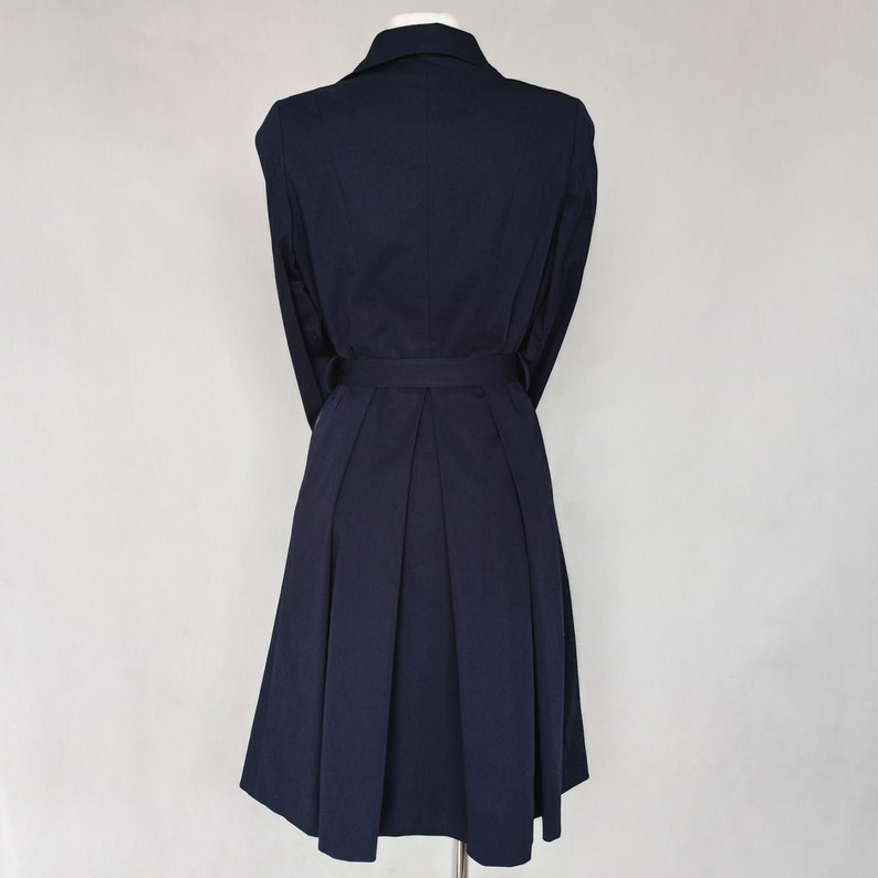 May include: A navy blue dress with a collared neckline, long sleeves, and a belt. The dress has a pleated skirt and a fitted bodice.