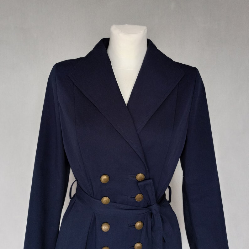 May include: A navy blue double-breasted coat with gold buttons and a belt.