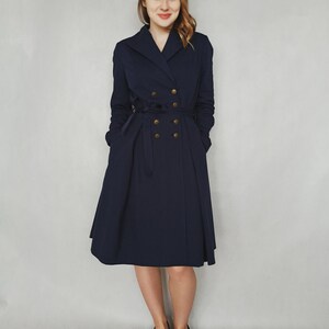 May include: A navy blue double-breasted coat with gold buttons and a belt. The coat has a flared skirt and is worn by a person with long brown hair.
