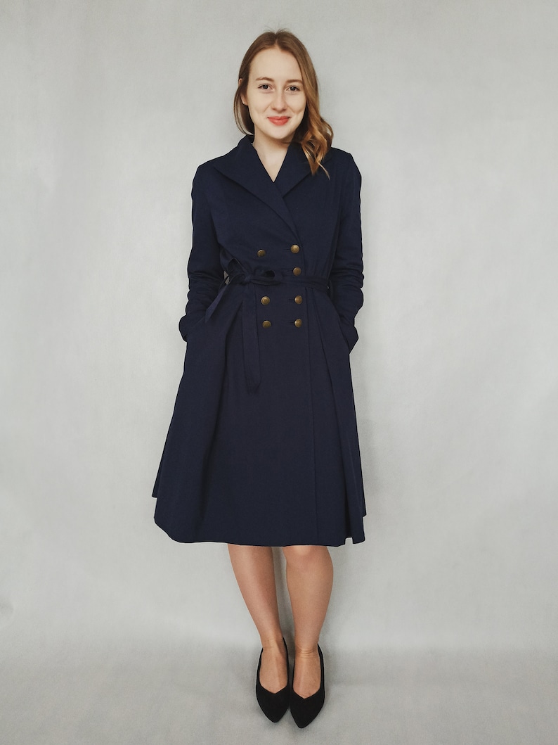 May include: A navy blue double-breasted coat with gold buttons and a belt. The coat has a flared skirt and is worn by a person with long brown hair.