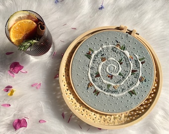 May include: A light blue embroidery hoop with a white spiral design and the text "The greatest gift is patience, accept the pace of your own unique world." The hoop is in a wooden frame.