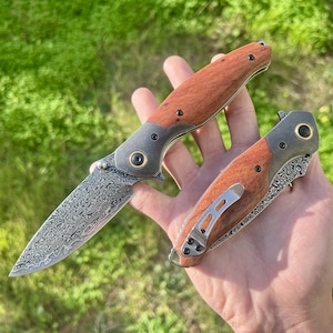 Könnte beinhalten: Zwei Klappmesser mit Holzgriffen und gemusterten Klingen werden gezeigt. Die Klingen haben ein einzigartiges, strukturiertes Design. Die Griffe sind warmbraun und die Metallakzente sind dunkelgrau. Ein Messer ist geöffnet, das andere ist geschlossen.