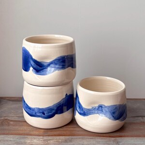 Cup with dimple in side for thumb and bold, wavy, blue brush stroke design