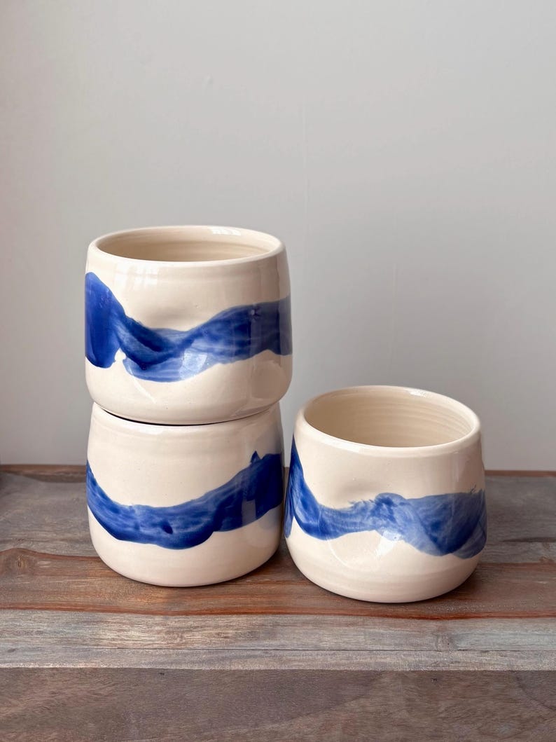 Cup with dimple in side for thumb and bold, wavy, blue brush stroke design