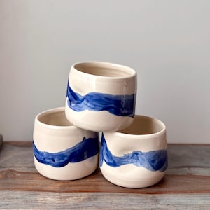 Cup with dimple in side for thumb and bold, wavy, blue brush stroke design