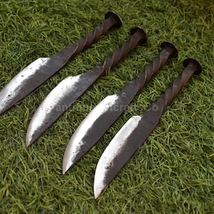 May include: Four handmade knives with twisted handles and curved blades. The blades have a silver finish, and the handles are dark brown. The knives are arranged diagonally on a bed of green grass.