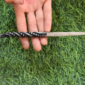 May include: A hand-forged letter opener with a twisted handle and a pointed blade. The handle features a decorative spiral design and a curled end. The metal has a dark, textured finish, and the blade is silver.