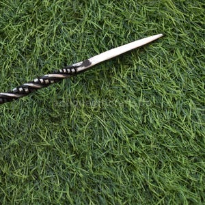 May include: A hand-forged, black and silver letter opener with a twisted handle and a pointed blade. The opener is lying on a bed of green grass.