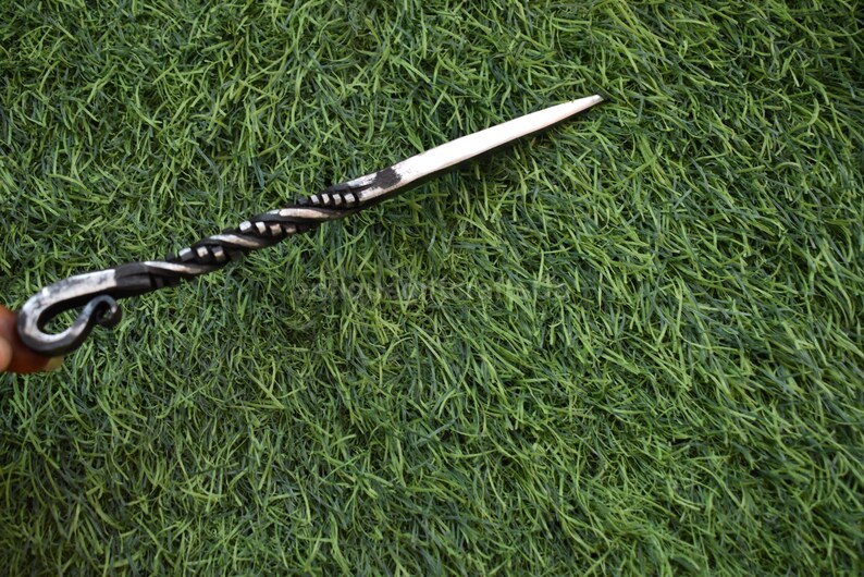 May include: A hand-forged, black and silver letter opener with a twisted handle and a pointed blade. The opener is lying on a bed of green grass.