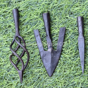 May include: Three different arrowheads made of metal. The arrowheads are on a green background.