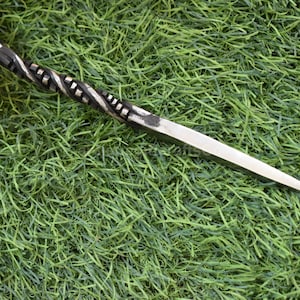 May include: A hand-forged metal awl with a twisted handle and a sharp, pointed blade. The awl is silver and black, and it is set against a green background.