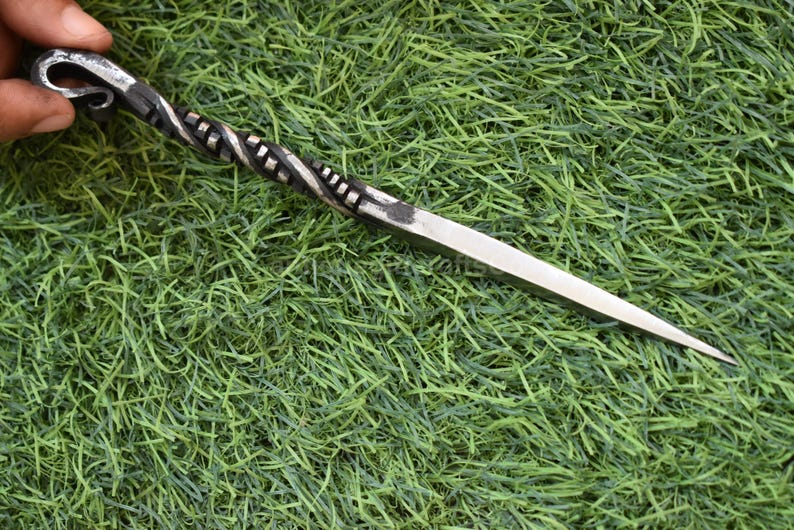 May include: A hand-forged metal awl with a twisted handle and a sharp, pointed blade. The awl is silver and black, and it is set against a green background.