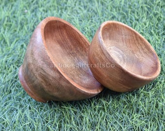 May include: Two wooden bowls with a natural wood grain finish are displayed on a bed of green grass. The bowls are different sizes and have a smooth, curved design. The text "antiquegiftcraftsCo" is visible on the bowls.