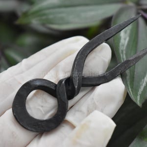 May include: A black metal hair fork with a twisted design and a circular loop at the base.