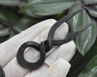 Puede incluir: Una horquilla para el pelo de metal negro con un diseño retorcido y un bucle circular en la base.