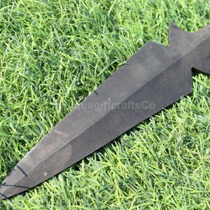 K&ouml;nnte beinhalten: Ein schwarzer Speerkopf mit einer Spitze und einem sternf&ouml;rmigen Design in der N&auml;he des Griffs. Der Speerkopf liegt auf einem Bett aus gr&uuml;nem Gras. Der Text "uegiftcraftsCo" ist sichtbar.