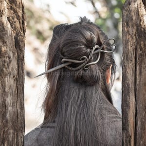 以下が含まれることがあります： ねじれたデザインの銀色の金属製のヘアピン。ピンは女性の髪をまとめたお団子に留めています。