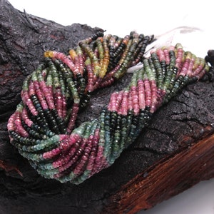 May include: A strand of multi-coloured tourmaline beads. The beads are faceted and have a mix of pink, green, and black colours. The beads are strung on a clear thread and are arranged in a loose, flowing pattern.