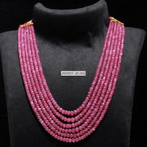 May include: A multi-strand necklace composed of small, faceted, pink beads. The necklace is displayed on a black mannequin bust. The text "BEADS BLING" is visible on the bust.