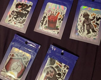 May include: Five sticker packs in clear plastic pouches with blue zip tops. Each pack contains holographic stickers with various horror-themed illustrations, including a ghost-faced figure, a bloody drink, and other spooky designs.