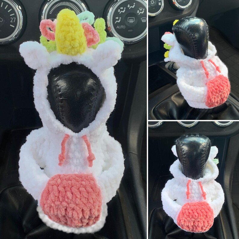 May include: White crocheted unicorn gear shift cover with a pink crocheted pom-pom. The unicorn has a yellow horn and rainbow mane.
