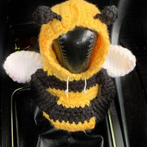 Peut inclure: Un pommeau de levier de vitesse de voiture en crochet en forme d'abeille. L'abeille porte un sweat &agrave; capuche jaune et noir ray&eacute; avec une capuche blanche. L'abeille a des yeux noirs et des ailes blanches.