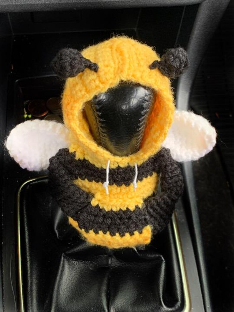 Peut inclure: Un pommeau de levier de vitesse de voiture en crochet en forme d'abeille. L'abeille porte un sweat &agrave; capuche jaune et noir ray&eacute; avec une capuche blanche. L'abeille a des yeux noirs et des ailes blanches.
