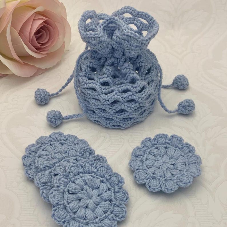 Puede incluir: Un conjunto de cuatro rondas de algod&oacute;n de crochet azul claro y una bolsa de cord&oacute;n de crochet azul claro con pompones.