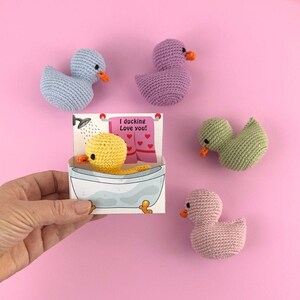 Puede incluir: Un conjunto de cinco juguetes de pato de crochet. Los patos son de varios colores, incluyendo morado, azul, verde, rosa y amarillo. El pato amarillo est&aacute; en una ba&ntilde;era con el texto "I duckin' love you!" en una tarjeta.