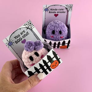 Puede incluir: Dos juguetes de peluche con tem&aacute;tica de Halloween en cajas decorativas. Uno es rosa con detalles morados y el texto "You are BOO-tiful!". El otro es morado con el texto "Kinda cute Kinda spooky". Ambos tienen ojos negros y sonrisas rosas.