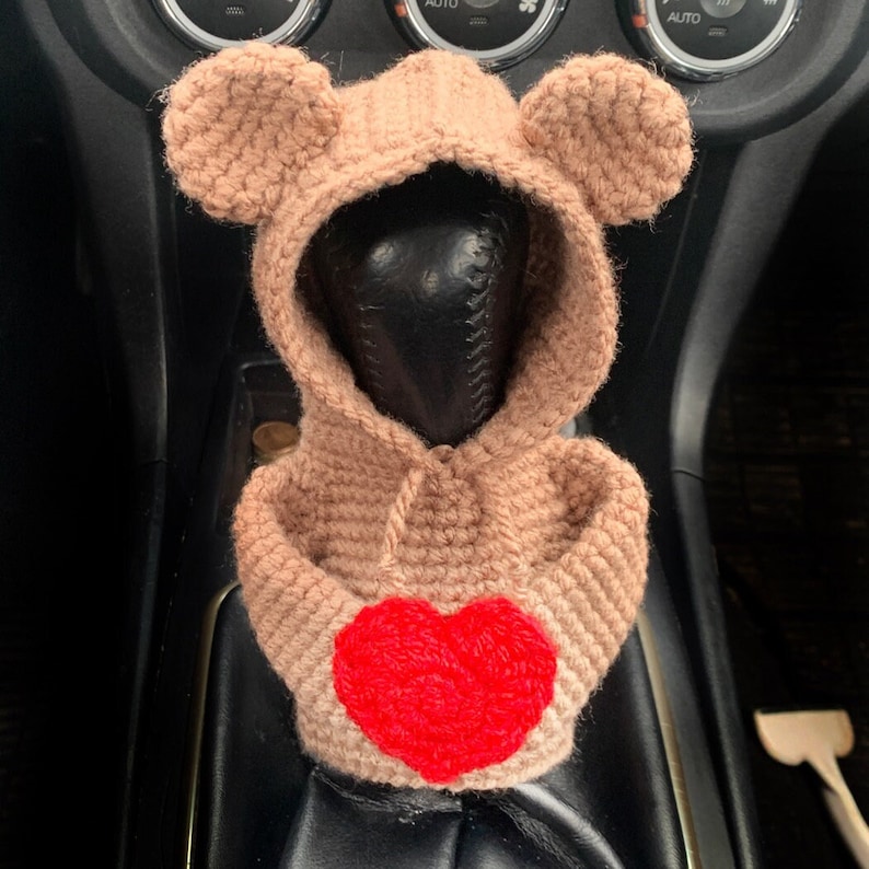May include: A brown crocheted bear-shaped car gear shifter cover with a red heart on the front.