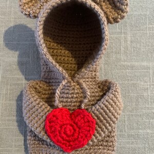 May include: A brown crocheted hooded sweater with bear ears and a red crocheted heart on the front.