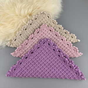 Puede incluir: Tres doilies triangulares de ganchillo en tonos beige, rosa y morado. Cada doily tiene un borde festoneado.